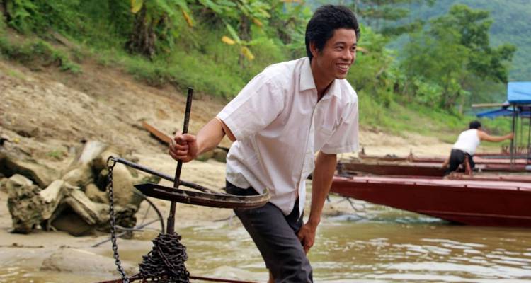 Mann, der auf einem Bootsruder auf einem Fluss steht.