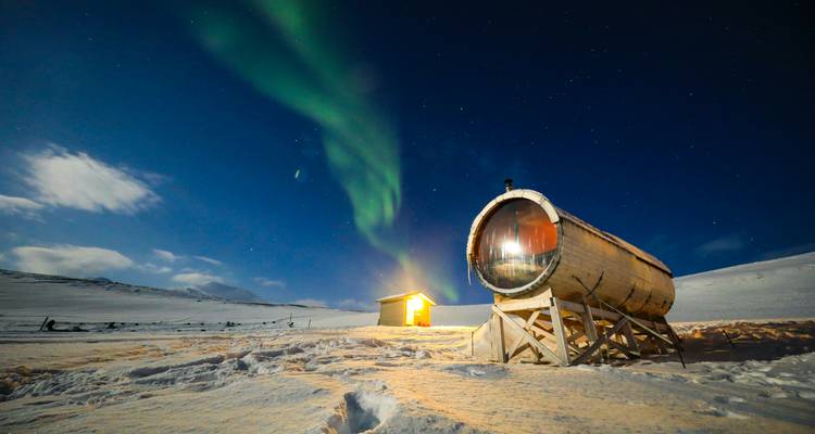 Aurora borealis over a small cabin in a snowy landscape.