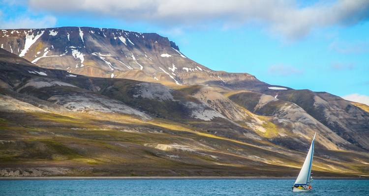 Sailboat in the waters off Svalbard with a mountain backdrop.