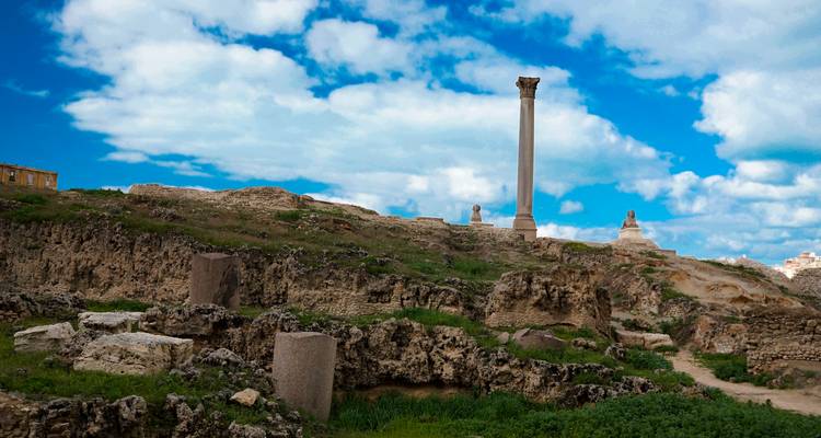Ancient ruins with a single standing column on a hill under a cloudy sky.