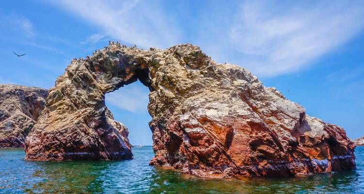 Un arco natural de roca en aguas azul vívido con aves en Paracas, Perú.