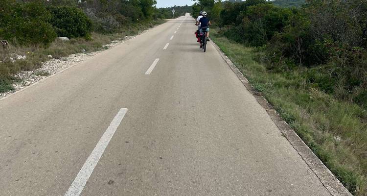 Personne faisant du vélo sur une longue route droite à travers un paysage rural.