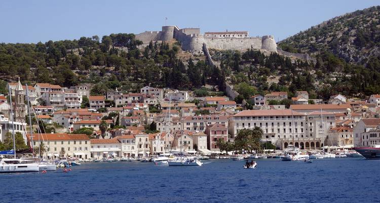 Ville côtière avec des structures historiques et une forteresse sur une colline.