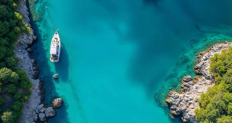 Vue aérienne d'un yacht ancré dans une baie bleu clair entourée de verdure.