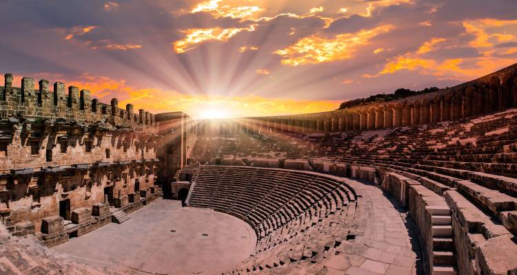 Vue panoramique large de l'amphithéâtre d'Aspendos sous un ciel de lever de soleil dramatique.