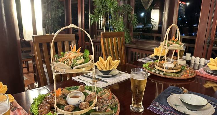 Elegant Vietnamese dining setup with bamboo baskets of assorted dishes, beer glass and tropical decor.
