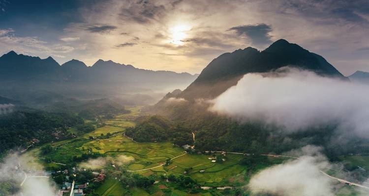 Misty sunrise over a lush valley of rice fields and jagged limestone mountains in northern Vietnam.