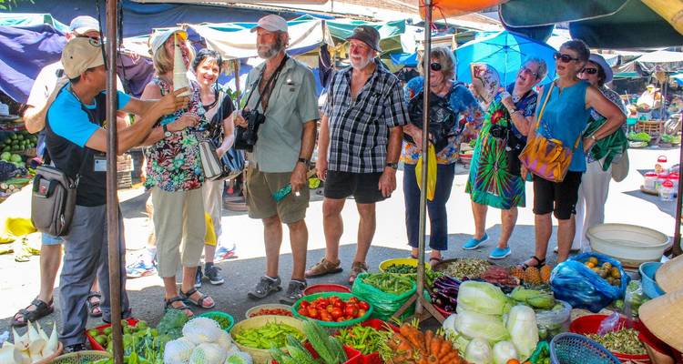 Tourists engage with a vibrant fresh produce market stall filled with colorful vegetables.