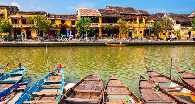 Colorful wooden boats line the canal facing Hoi An's vibrant yellow shophouses decorated with lanterns.