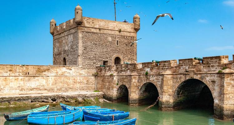 Versterkte muren en blauwe boten in de haven van Essaouira.