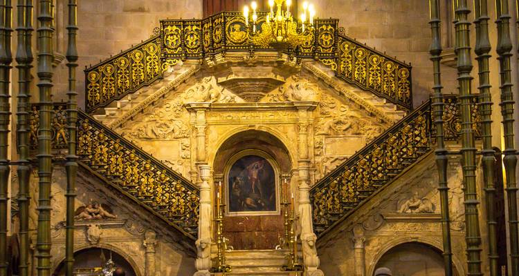 Weelderige vergulde trappen en stenen beeldhouwwerken sieren het rijkelijk verlichte interieur van de Kathedraal van Burgos.