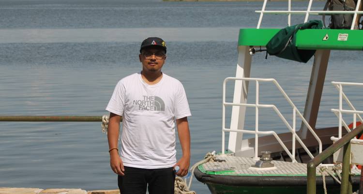 Traveler standing beside a small green boat at a lakeside pier on a bright day.