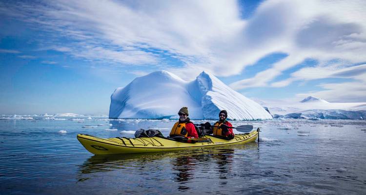 Two people kayaking among icebergs in Antarctica.