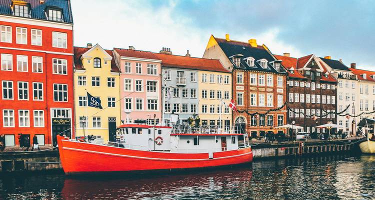 Barco de pesca rojo amarrado junto a casas de colores pastel en el canal Nyhavn de Copenhague bajo una luz suave