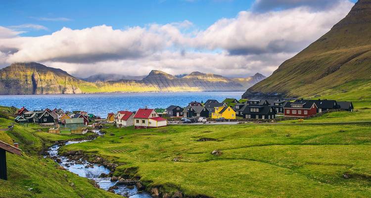 Pintoresco pueblito costero de casas coloridas frente a un fiordo bajo los dramáticos acantilados de las Islas Feroe.