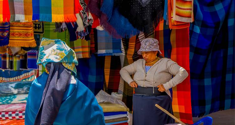Vrouwen die kleurrijke geweven dekens en textiel schikken bij een buitenmarktkraam