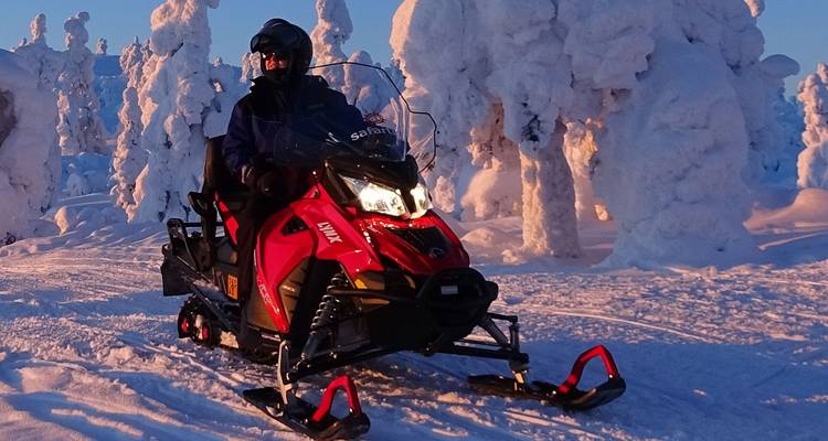 A rider navigates a red snowmobile through a frozen forest of heavily frosted trees at sunrise.