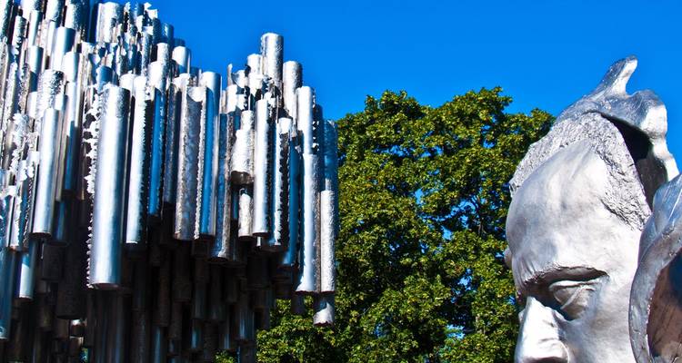 Detail of Helsinki’s Sibelius Monument metal pipes beside the composer’s sculpted face under blue sky.