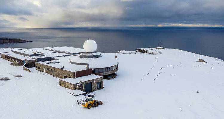 Eine verschneite Landschaft mit einer Radarstation mit Blick auf den Ozean.