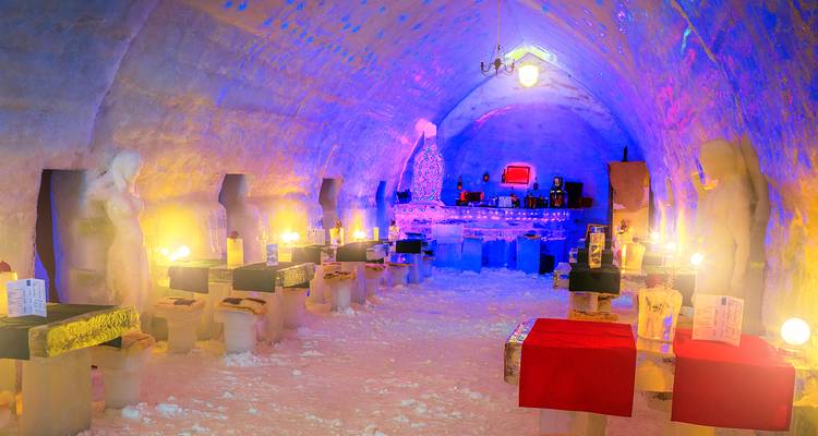 Farbenfrohe beleuchtete Eisbar, die in einen Schnee- und Eistunnel geschnitzt ist, mit Tischen und Skulpturen.