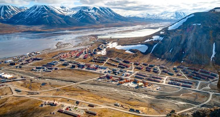 Vue aérienne d'un village arctique avec des maisons colorées s'étendant sous des montagnes enneigées et un large fjord.