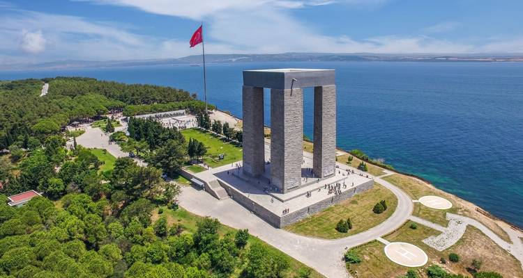 Large memorial monument with a Turkish flag by the sea.