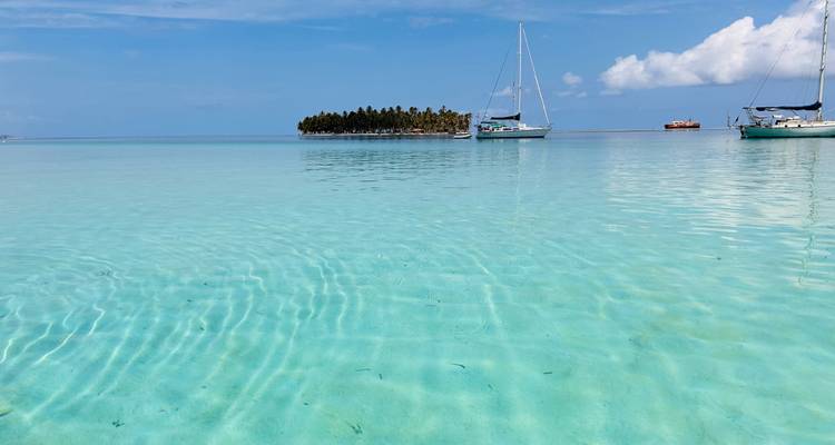 Eaux turquoise limpides avec petite île et bateaux.