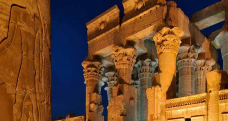 Detail of ancient Egyptian columns at night, illuminated by lights.