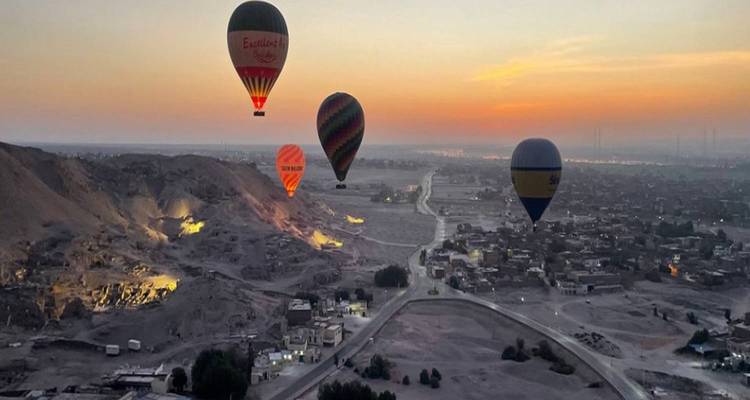 Heteluchtballonnen boven een landschap bij zonsopgang.