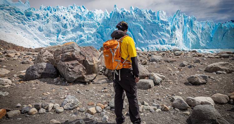 Traveler exploring rocky terrain with a giant glacier in view.