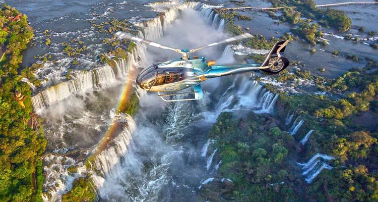 Helicopter flying over Iguazu Falls with a rainbow visible.