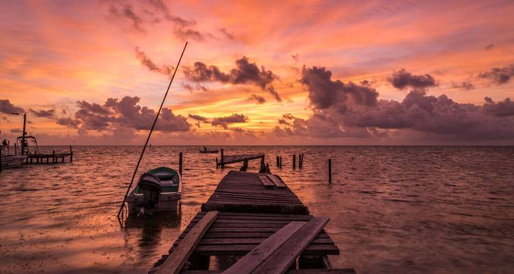 A wooden dock leading into the water with a vibrant sunset sky.