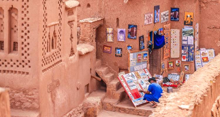 El artista con la bata azul pinta escenas coloridas en los muros de adobe de Ait Benhaddou.