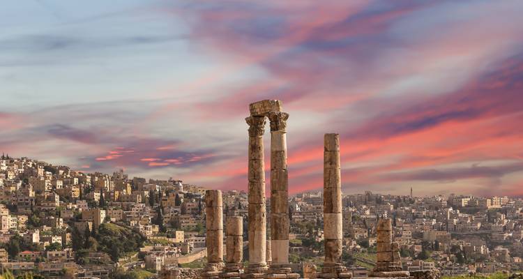 Tall Roman columns of the Temple of Hercules with Amman cityscape under colorful sky
