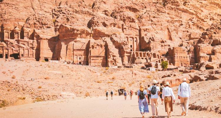 Visitors walking the sandy entrance valley toward rock-hewn façades of Petra