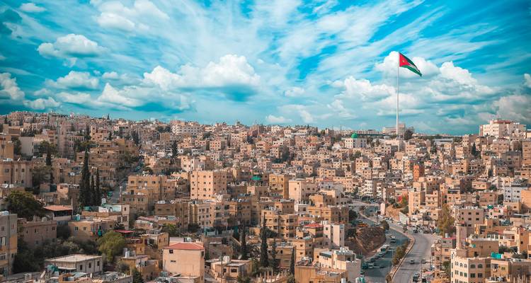 Panoramic skyline of Amman with giant Jordanian flag under dramatic blue sky