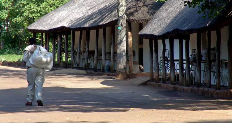 A person carrying a bag along a path by traditional thatched-roof buildings.