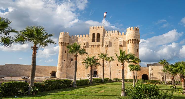 Historical fort with palm trees in Alexandria under a clear sky.