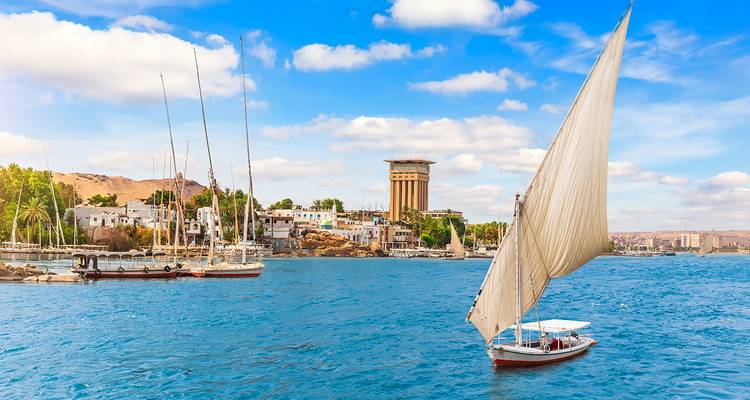 Nile River with traditional sailboat and modern buildings in the distance.