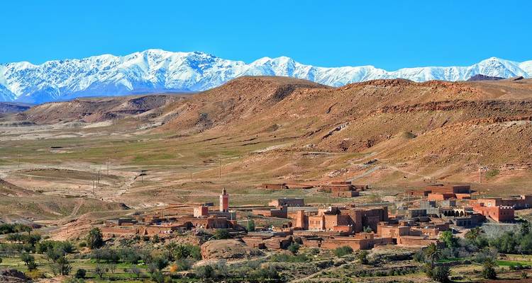 Zicht op Marokkaans dorp met besneeuwde bergen op de achtergrond.