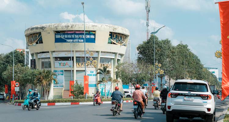 Busy street with motorbikes, cars, and a round building.