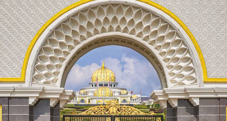 El arco decorativo enmarca perfectamente las cúpulas doradas del Palacio Nacional de Malasia bajo un cielo azul