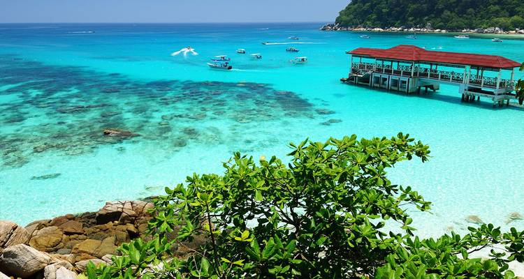 Laguna de las Islas Perhentian de color turquesa con parches de coral, botes y un muelle de madera