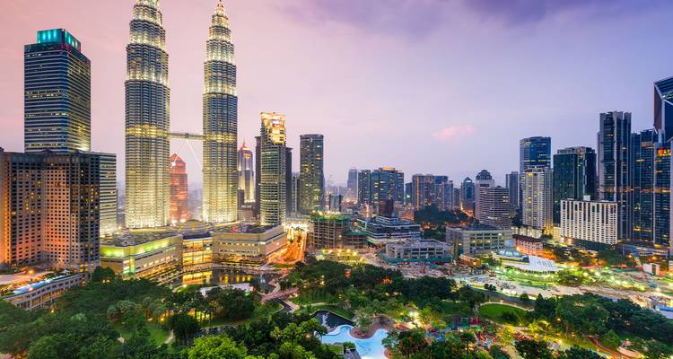 Torres Petronas gemelas y el horizonte de Kuala Lumpur brillando al atardecer sobre un parque urbano con jardines diseñados