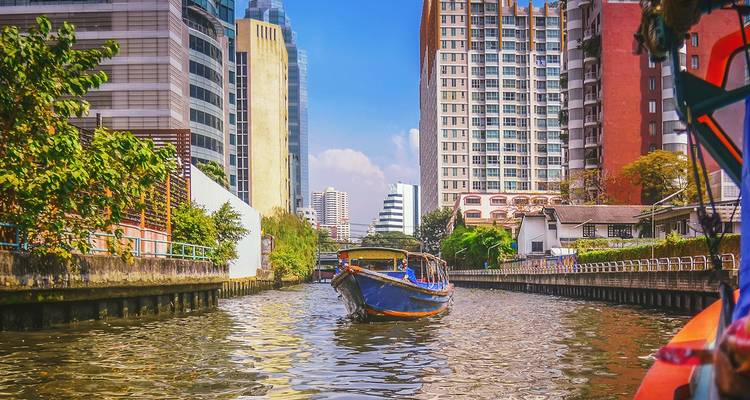 Een kanaal in een stedelijk gebied met een boot en hoge gebouwen op de achtergrond.