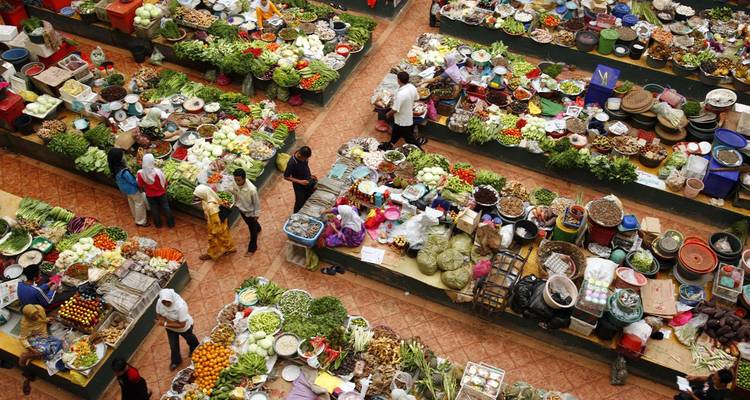 Mercado interior bullicioso visto desde arriba con productos coloridos y compradores en cada puesto.
