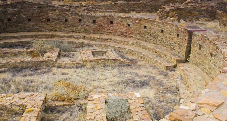 Anciennes ruines de pierre avec des formations circulaires envahies par l'herbe sèche.