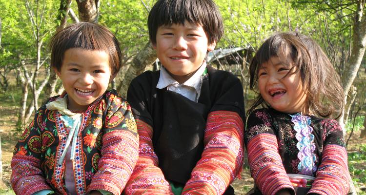 Tres niños sonrientes vistiendo ropa tradicional.