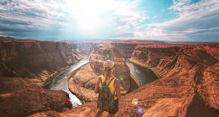 Joven viajero mirando hacia Horseshoe Bend donde el río Colorado se curva a través de paredes de cañón rojo empinadas.