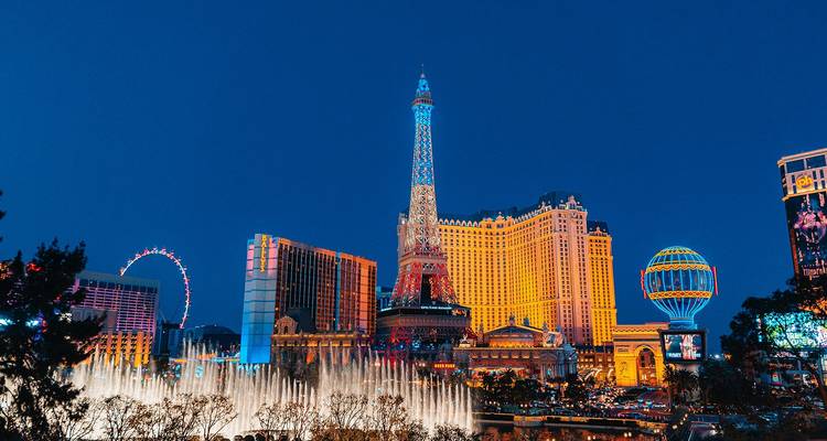 La Strip de Las Vegas de noche con fuentes y hoteles temáticos iluminados brillantemente.